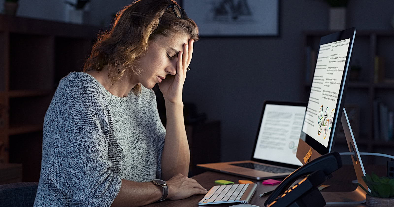 Mature and tired businesswoman working on computer until night. Portrait of a casual stressed lady with headache at desk.